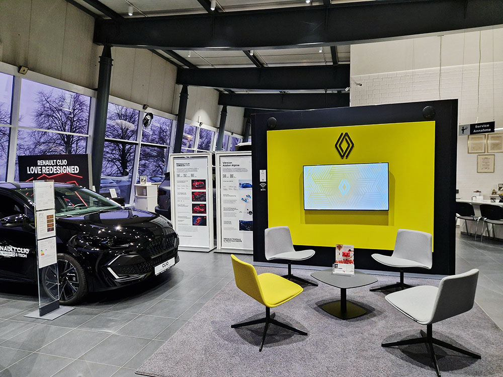 Automobile Clever Service Renault-Showroom mit ausgestelltem Clio, Sitzbereich mit gelben und weißen Stühlen sowie großer Renault-Wand mit Bildschirm.
