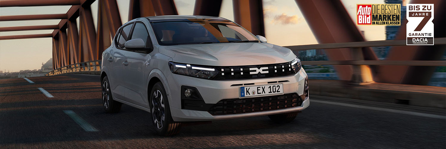 Jetzt ab 12.790 oder mit 0% Leasing Ein aktueller Dacia Sandero in elegantem Grau bei der Überquerung einer markanten roten Stahlbrücke.