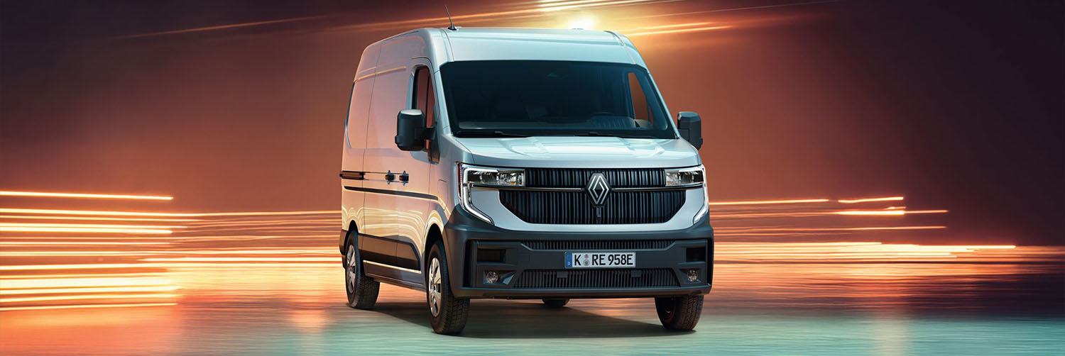 Ein silberner Renault Transporter steht in einer dynamisch beleuchteten Kulisse mit orangefarbenen Lichtstreifen. Das Nutzfahrzeug ist frontal aus leicht seitlicher Perspektive zu sehen und zeichnet sich durch einen markanten Kühlergrill, das Renault-Logo und schwarze Stoßfänger aus.
